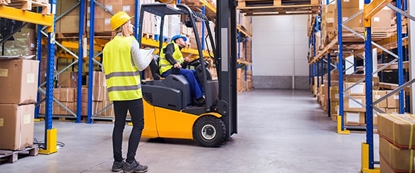 Young workers working together. Man forklift driver and a woman in a warehouse.