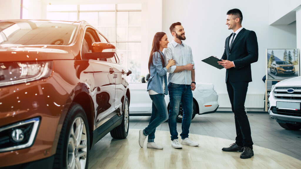 Car sales consultant talking to customers inside a dealership showroom.