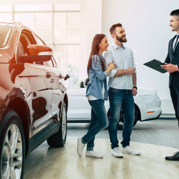 Car sales consultant talking to customers inside a dealership showroom.