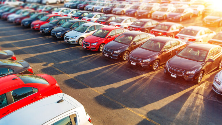 Rows of new cars parked outside a dealership on a sunny day.