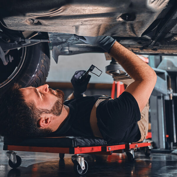 Mechanic on a creeper working under a raised car in a workshop.