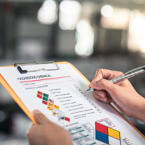 Person holding a clipboard and pen, reviewing a hazardous chemical form with safety symbols.