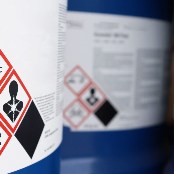 Containers with hazard pictograms showing corrosion, toxicity, and health risks.