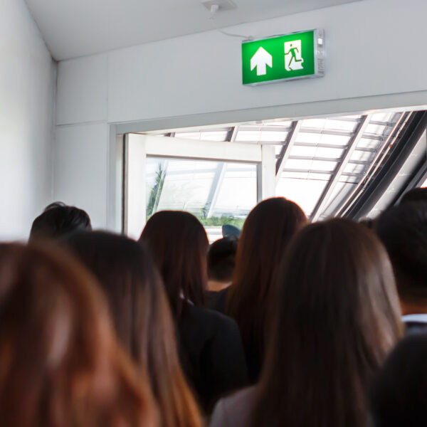 Group of people exiting a building through a door under a green emergency exit sign.