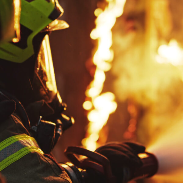 Firefighter in protective gear spraying water on flames.