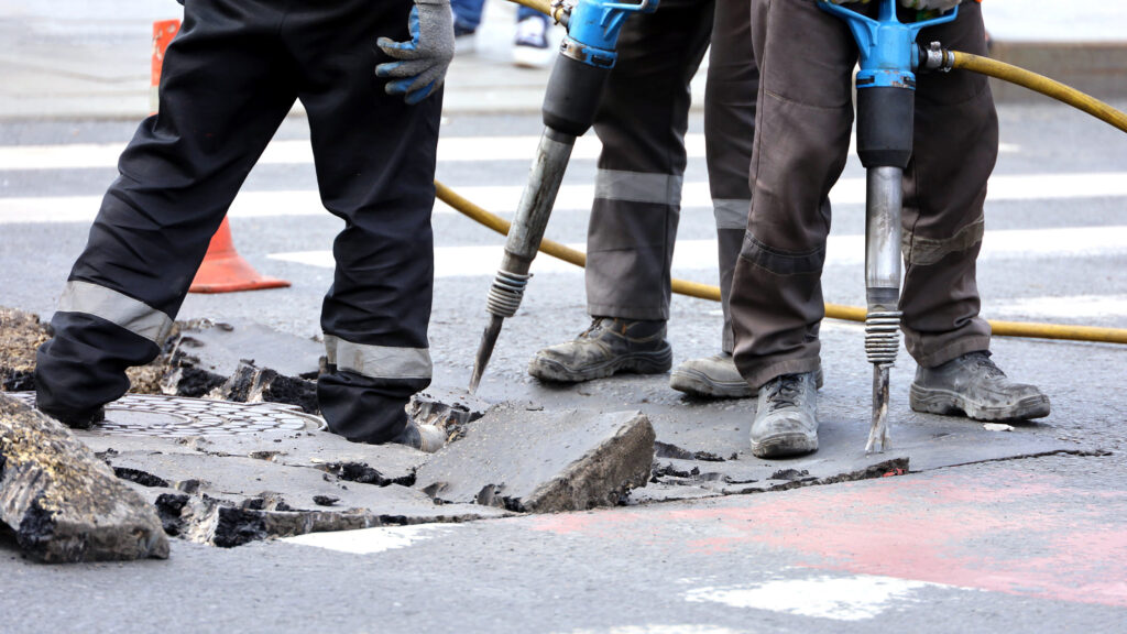 Close-up of workers operating pneumatic drills on a road surface.