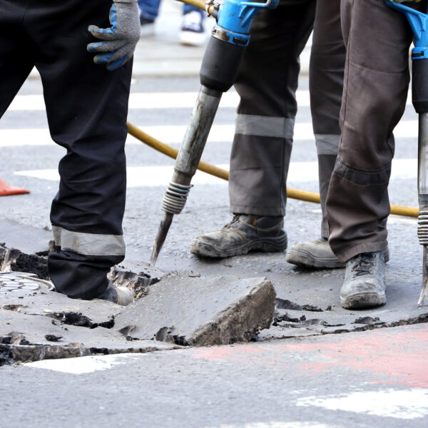 Close-up of workers operating pneumatic drills on a road surface.