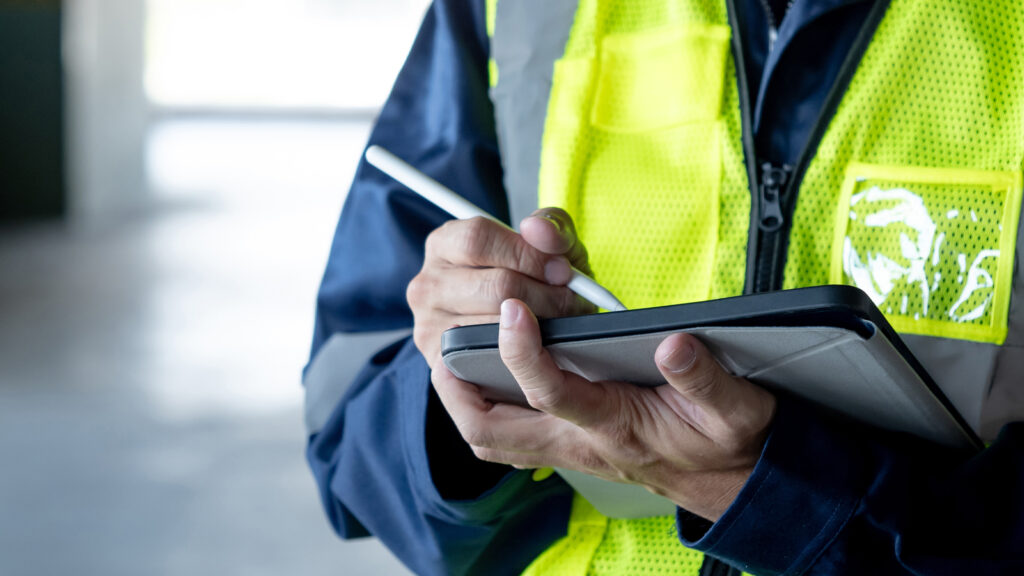 Person wearing a high-visibility vest using a tablet device to record information during a building inspection.