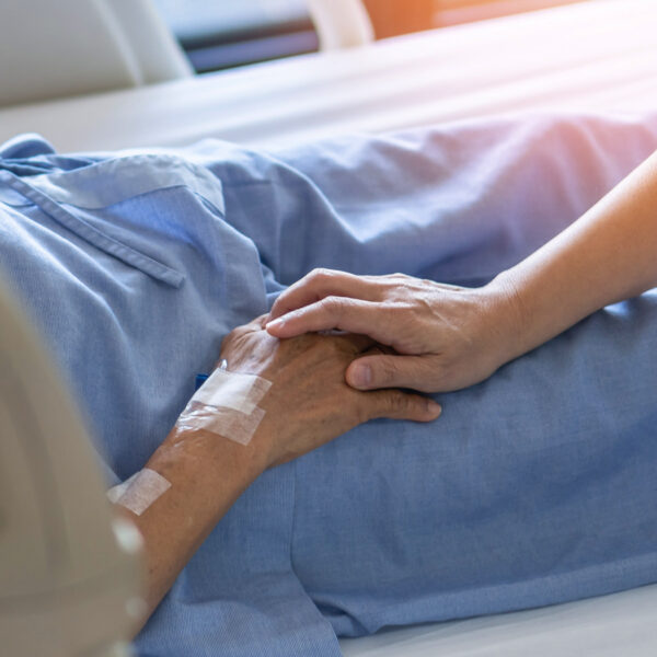 Healthcare worker holding a patient’s hand in a hospice bed.