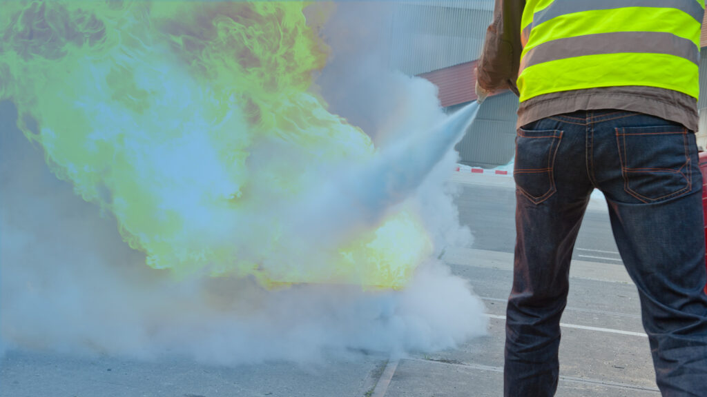 Worker wearing a PPE standing on a road while releasing a fire extinguisher to extinguish fire.