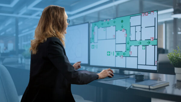 Office worker reviewing a digital building floor plan with evacuation routes displayed on multiple computer screens.
